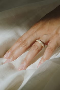 a woman's hand with a wedding ring on top of her finger, resting on a white sheet