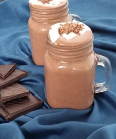 two mason jars filled with chocolate and marshmallows on a blue table cloth