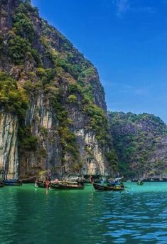 several boats floating on the water in front of large mountains and cliffs with blue sky