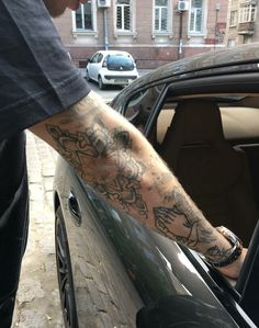 a man with tattoos on his arm getting out of a car