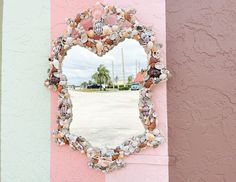 a heart shaped mirror mounted to the side of a pink and white wall next to a parking lot