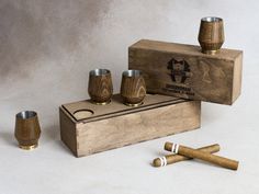 a wooden box with three shot glasses and two cigars on the table next to it