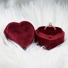 a red velvet ring box with a heart shaped diamond in it sitting on white fur