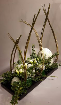 an arrangement of plants and eggs on a black tray with white flowers in the center