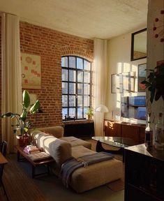 a living room filled with furniture next to a brick wall and large windows in the background