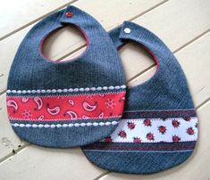 two baby bibs with red and blue designs on them sitting on a wooden floor