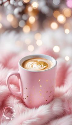 a cup of coffee on top of a pink fuzzy surface with lights in the background