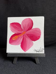 a painting of a pink flower on a white canvas with black stand and dark background