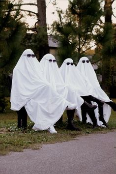 three people in white ghost costumes sitting on a bench