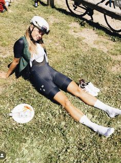 a woman laying on the ground next to a white frisbee and bike helmet