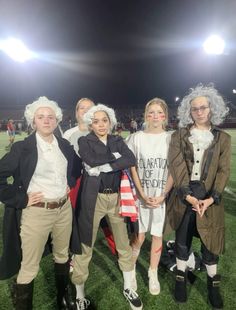 four people dressed in costumes standing on a field at night with an american flag behind them