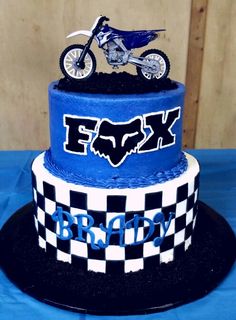 a blue and white cake with a dirt bike on it's top, sitting on a table