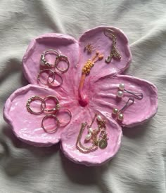 a pink flower with lots of rings and jewelry on it's center, sitting on top of a white sheet