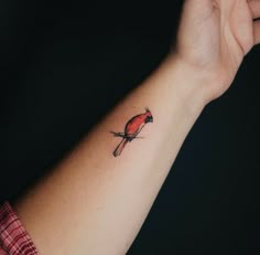 a small red bird tattoo on the left wrist and right arm, with a black background