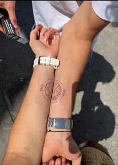 two people holding hands with tattoos on their arms and wristbands, both showing the same symbol