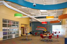 the inside of a school with tables and chairs on each side of the room, lights hanging from the ceiling