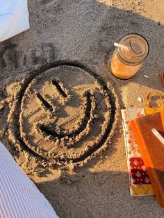 a smiley face drawn in the sand next to other items