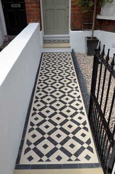 a black and white tiled walkway leading up to a front door with a potted plant