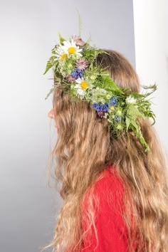 a woman with long hair wearing a flower crown in front of her face and back to the camera