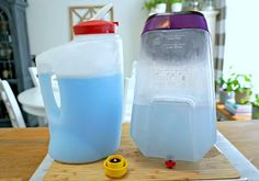 two plastic jugs sitting on top of a wooden table next to a yellow cup