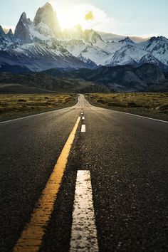 an empty road with mountains in the background and sun shining down on it's sides