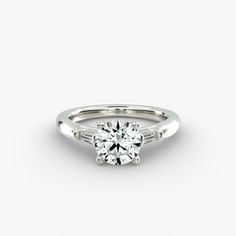 a white gold engagement ring with two baguets on each side and a round brilliant diamond in the center