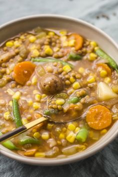 a bowl filled with soup and vegetables on top of a blue table cloth next to a wooden spoon