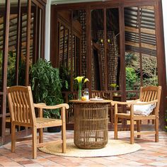 two wooden chairs sitting on top of a brick floor next to a table with flowers