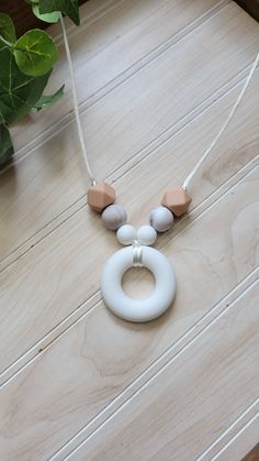 a white necklace with three different colored beads on a wooden table next to a potted plant