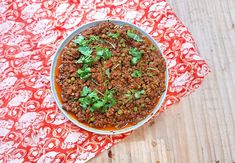 a bowl filled with food sitting on top of a red and white table cloth next to a wooden cutting board