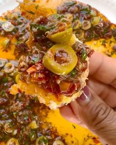 someone holding up a piece of food with olives and other toppings on it