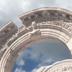 an arch with statues on it and clouds in the sky behind it, as seen from below