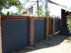 a wooden fence with metal slats in front of a brick wall and trees on the other side