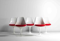 four white and red chairs sitting next to each other in front of a white wall