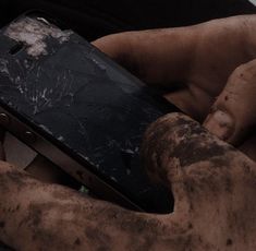 a person holding a cell phone in their hands with dirt all over the screen and on it's side