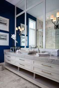 a bathroom with blue walls and marble counter tops, two sinks and mirrors on the wall