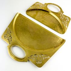 two brass trays with handles on each side, one has an oval handle and the other has a flower design