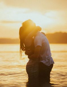 a couple kissing in the water at sunset