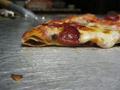 a slice of pepperoni pizza sitting on top of a metal counter next to a spatula