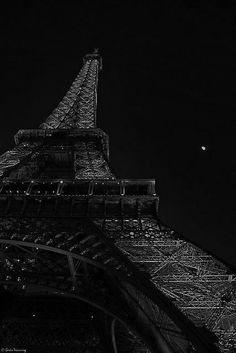 the eiffel tower lit up at night in black and white with an airplane flying by