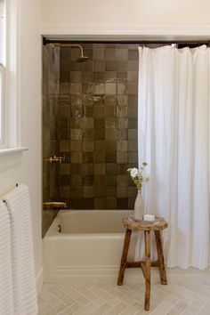 a white bath tub sitting under a window next to a wooden stool with flowers in it