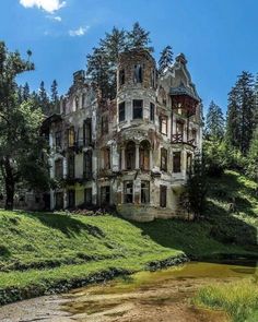 an old abandoned house sitting on top of a lush green hillside next to a river