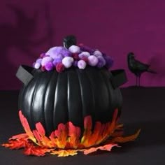 a black teapot with purple and orange flowers in it sitting on a table next to a bird