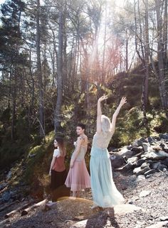 three women standing on top of a rocky hillside next to trees and rocks with their arms in the air