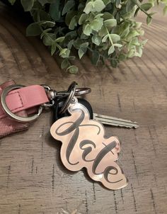 a keychain with the letter g on it sitting next to a flower pot