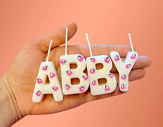 a hand holding three small candles with the word baby spelled out in pink and white frosting