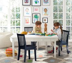 two children are sitting at a table with books in front of them and looking at pictures on the wall