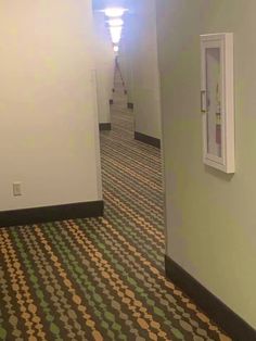 an empty hallway with a clock on the wall next to a door and carpeted floor