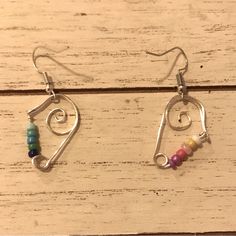 two pairs of earrings with colorful beads hanging from them on a wooden surface, one is made out of metal and the other has a spiral design