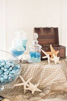 a table topped with blue candies and starfish next to a trunk filled with candy